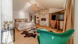 A modern bedroom with a large bed, a fireplace, a TV, and a green armchair.