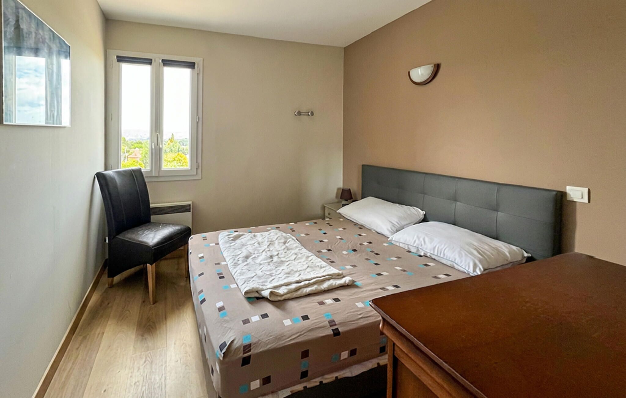 A bedroom with a bed, a chair, a bedside table, a lamp, and a window with a view.