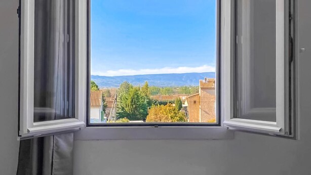 Une fenêtre donnant sur un quartier résidentiel, avec des maisons et des arbres, sous un ciel bleu dégagé.