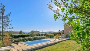 Une piscine dotée d’une terrasse dallée, entourée d’une pelouse verdoyante et d’arbres.