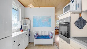 Eine kompakte Küche mit weißen Schränken, einer eingebauten Mikrowelle und einem Backofen. Eine Weltkarte hängt an der Wand, und eine kleine Bank mit Kissen lehnt an der Wand.