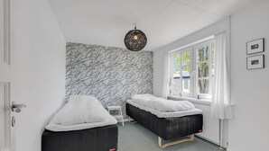 Ein Zimmer mit zwei Betten, einer Wand mit Muster, einer Pendelleuchte und einem Fenster mit Vorhängen.