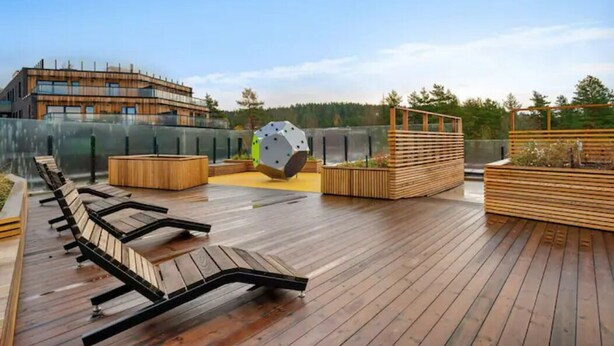 Eine Holzterrasse mit Liegestühlen, einer großen, kugelförmigen Skulptur und einem modernen Gebäude im Hintergrund.