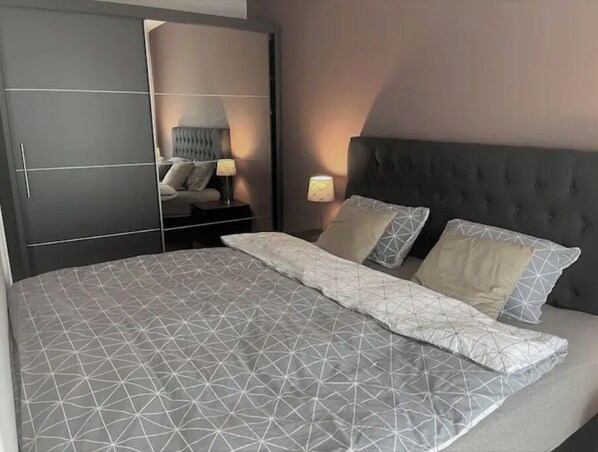 A bedroom with a large bed, a dark headboard, and a wardrobe with mirrored doors.