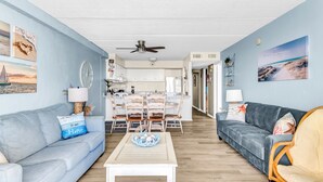 A living room with a sofa, a coffee table, and a dining area with chairs and a table. - Charming Oceanfront Condo, 2 Open private balconies (Ocean City)