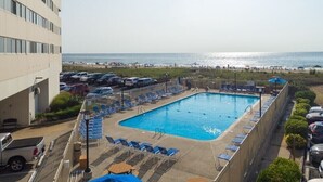 A swimming pool with lounge chairs, a parking lot, and a view of the beach and ocean. - Charming Oceanfront Condo, 2 Open private balconies (Ocean City)