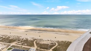 A beach view with a clear sky, sandy beach, and a fenced area with solar panels. - Charming Oceanfront Condo, 2 Open private balconies (Ocean City)