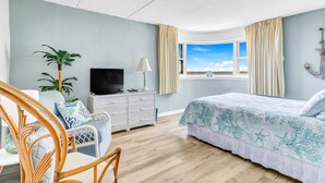 A bedroom with a bed, a TV, a plant, and a window with curtains. - Charming Oceanfront Condo, 2 Open private balconies (Ocean City)
