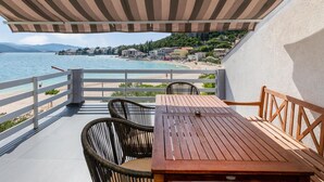 Eine Terrasse mit Holztisch und -stühlen mit Blick auf einen Strand und eine Küstenstadt.