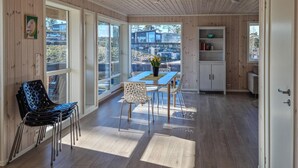 A modern interior with a wooden ceiling, large windows, a dining area with a table and chairs, and a white cabinet with books. - 4 bedroom amazing home in Færvik (Færvik)