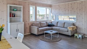 A cozy living room with a sectional sofa, a coffee table, a bookshelf, and large windows offering a view of the outdoors. - 4 bedroom amazing home in Færvik (Færvik)