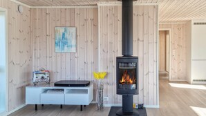A modern living room with a wood-paneled wall, a white entertainment unit, a black wood-burning stove, and a painting above the unit. - 4 bedroom amazing home in Færvik (Færvik)