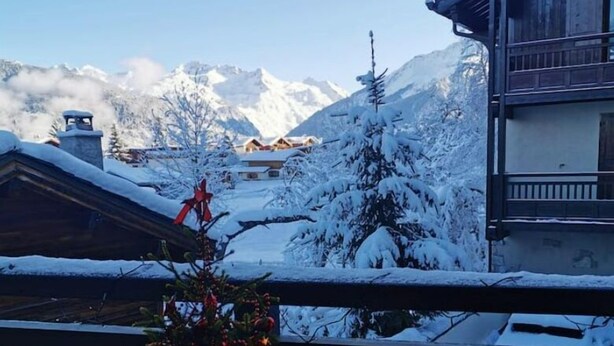Ein Balkon mit Tisch und Stühlen, mit Blick auf eine verschneite Berglandschaft mit Gebäuden.