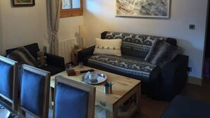Ein gemütliches Wohnzimmer mit einem gemusterten Sofa, einem Holztisch und einem gerahmten Bild an der Wand.