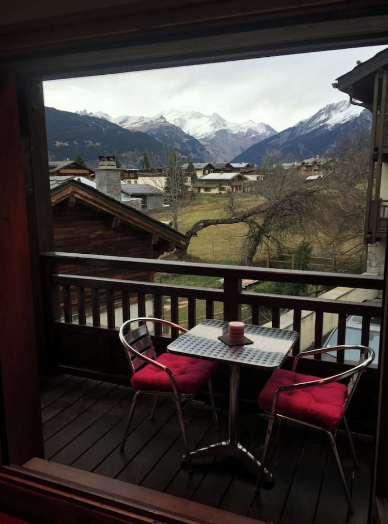 A balcony with a table and two chairs, overlooking a mountainous landscape with buildings in the valley.