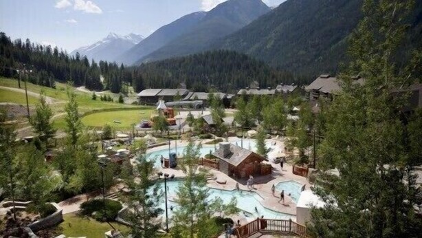 Un resort con varias construcciones, un área de piscina y un paisaje montañoso de fondo.