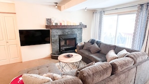 Una sala de estar moderna con un sofá modular, una chimenea, un televisor de pantalla plana y un amplio ventanal con cortinas.
