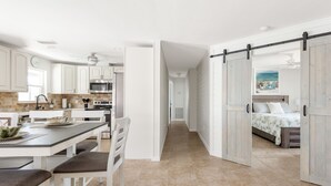 A modern kitchen with white cabinets, a dining area with a bench, and a bedroom with a bed and a view of the beach. - Nature's Splendor! Lovely Setting. (Rotonda West)