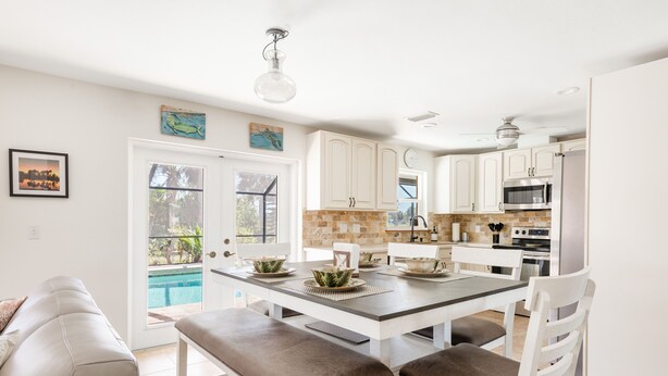 A modern kitchen with white cabinetry, a central island with stools, a built-in oven, and a view of a swimming pool. - Nature's Splendor! Lovely Setting. (Rotonda West)