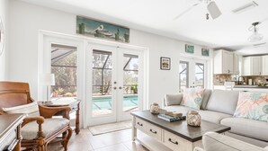 A spacious living room with a large window, a dining area with a wooden table, and a kitchen with white cabinets. - Nature's Splendor! Lovely Setting. (Rotonda West)