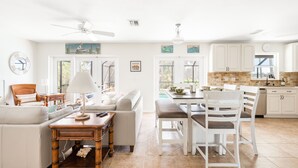 A bright living room with a sofa, a wooden table, and a dining area with chairs. There is a kitchen with white cabinets and a window. - Nature's Splendor! Lovely Setting. (Rotonda West)
