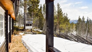 Mökki, jonka ulkoseinät ovat puuta, maasto on lumen peitossa ja näköala avautuu metsäiselle vuoristolle.