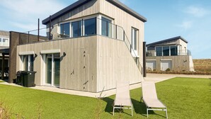 Een modern gebouw met twee verdiepingen, een plat dak, grote ramen en een overdekt terras met een lounge stoel.