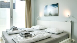 Een moderne hotelkamer met een groot bed, twee kussens, een netjes gevouwen handdoek en een kunstwerk aan de muur.