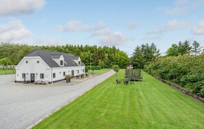 A white building with a sloped roof, a gravel driveway, and a well-maintained lawn with outdoor seating.