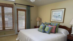 A bedroom with a large bed, a door with a curtain, a framed picture on the wall, and a nightstand with a lamp.