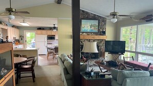 A spacious living room with a sofa, a coffee table, and a television. There is a dining area with a table and chairs, and a kitchen in the background.