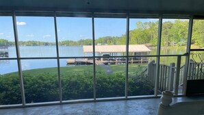 A room with large windows overlooking a lake, a dock, and a grassy area with a building in the background.