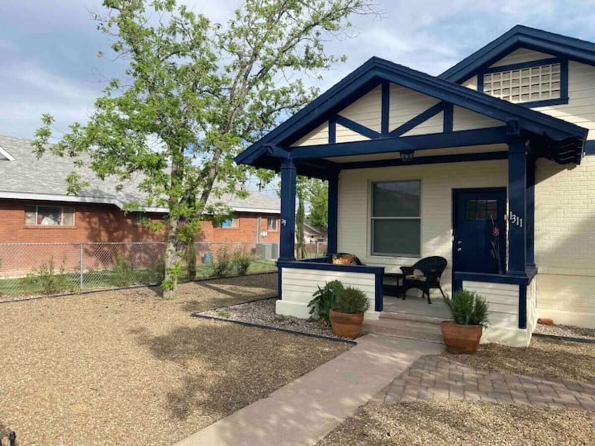 A house with a blue and white exterior, a front porch with two potted plants, and a small seating area.