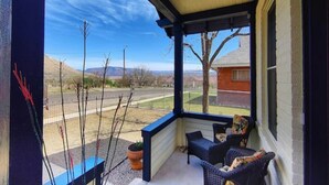Eine überdachte Veranda mit Blick auf einen umzäunten Garten und ferne Berge.