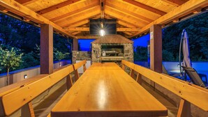 Una terraza exterior de madera con chimenea de piedra, bancos y una mesa.