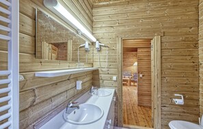 Une salle de bain rustique, avec des murs en bois, comprenant deux lavabos, un miroir et un espace douche.