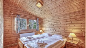 Une chambre dans un chalet en bois, avec deux lits, une fenêtre avec des rideaux et un radiateur.