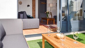 Un espacio al aire libre moderno con un sofá gris, una mesa de madera y dos copas de vino.