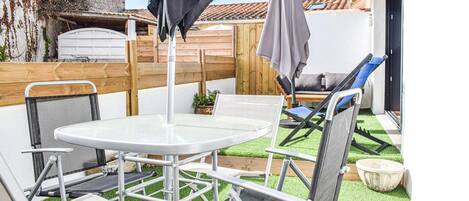A patio with a round table, two chairs, a blue lounge chair, and a small potted plant.