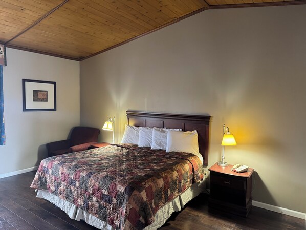 A neatly arranged bedroom with a large bed, two bedside lamps, a chair, and a framed picture on the wall. - Town & Country Motel (Clinton)