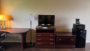 A hotel room with a desk, a television, a lamp, a dresser, and a coffee maker.