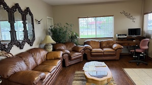 A living room with leather sofas, a wooden coffee table, a lamp, and a large window with blinds.