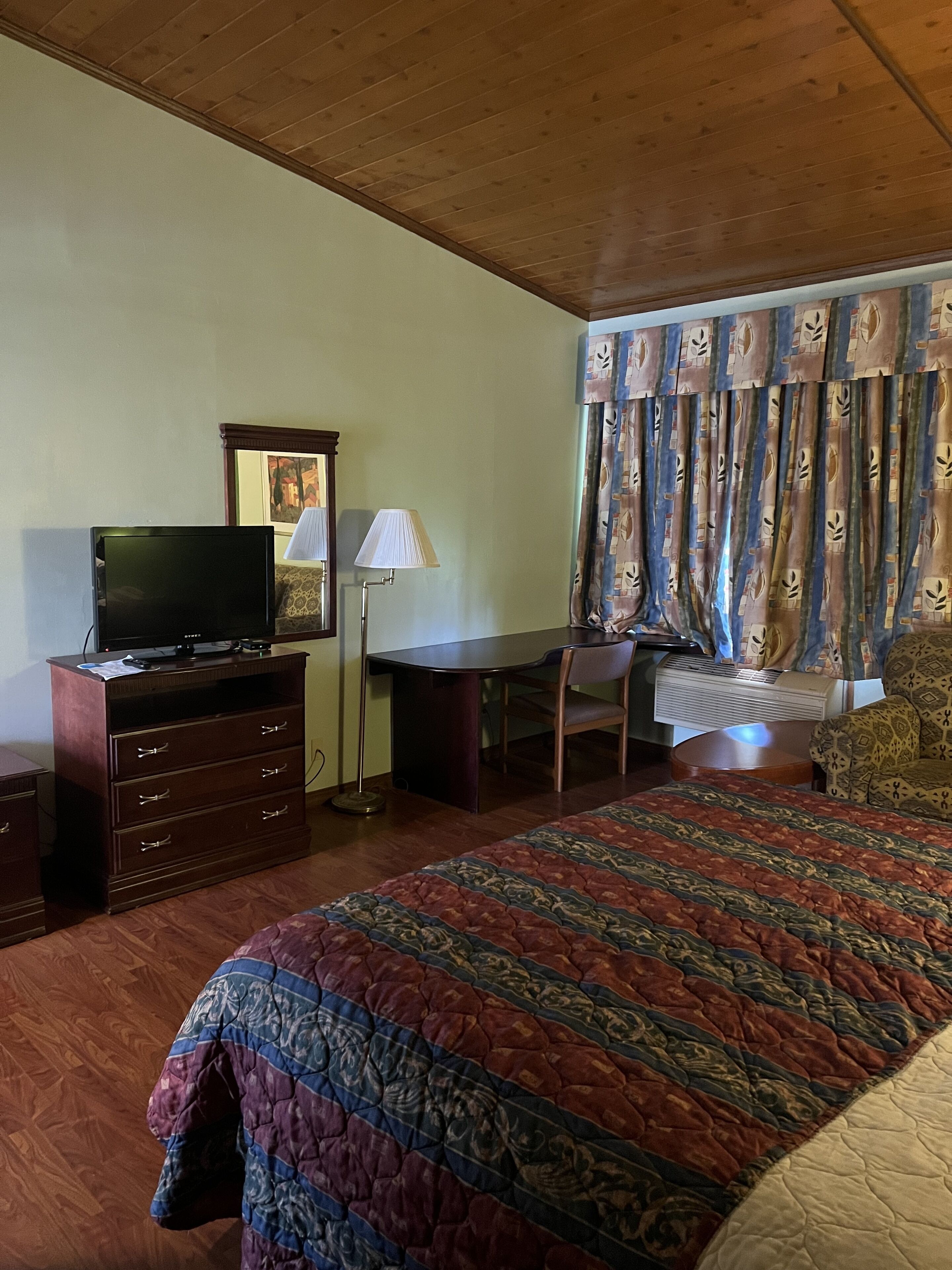 Un dormitorio con una cama, un escritorio, una silla, un televisor y una lámpara.