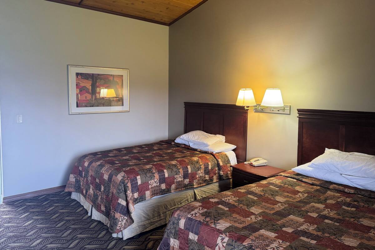 A hotel room with two beds, a wooden ceiling, a framed picture on the wall, and bedside lamps.
