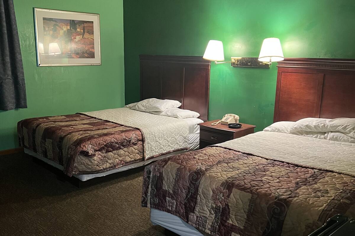 A hotel room with two beds, green walls, wooden ceiling, and a painting on the wall.
