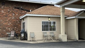 A small, single-story building with a brick exterior and a beige siding exterior. There is a covered outdoor seating area with a table and chairs.