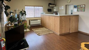 A spacious room with a wooden floor, a large window with blinds, a wooden reception desk, a clock on the wall, and a "No Smoking" sign.