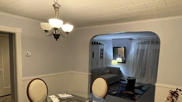 Ein Essbereich mit einem runden Glastisch, vier Stühlen, einer Pendelleuchte, einer Couch und einer Lampe im Hintergrund.