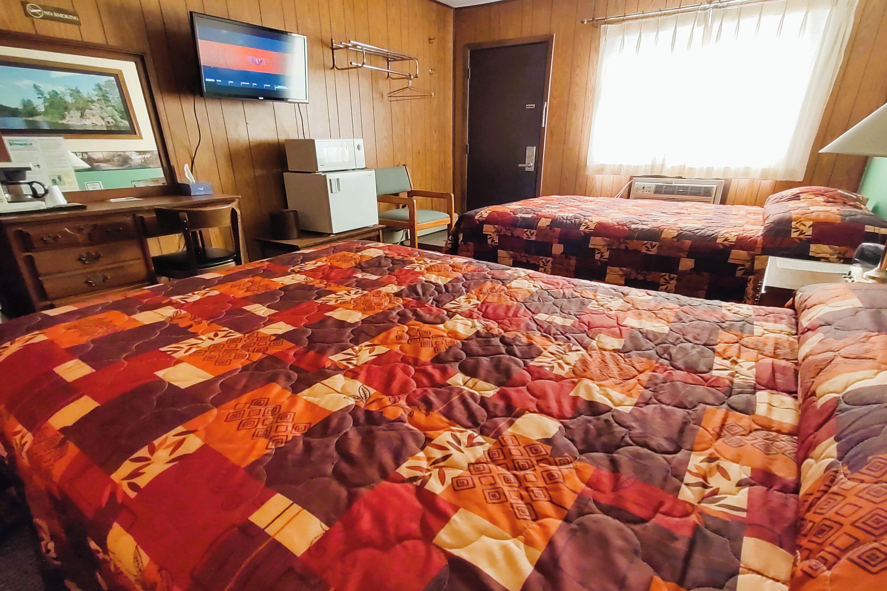 A hotel room with two beds, a desk with a computer, a television, and a door.