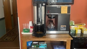 Una estación de café con una cafetera, un dispensador de té y un televisor montado encima.